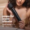 A woman in a satin top holds a black plug-in vibrating wand massager