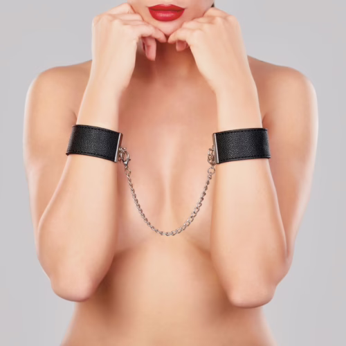 Black wrist cuffs with connector chain, worn by a model with red lips