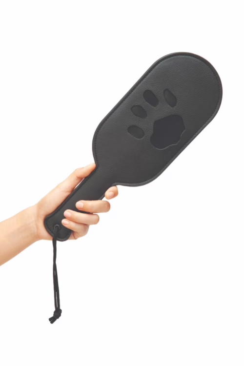 A hand holding a black paddle with a paw print cutout
