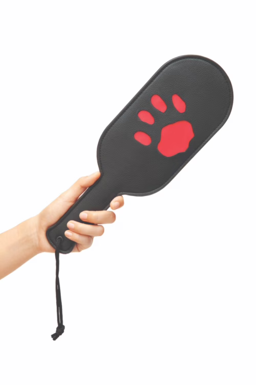 A hand holding the Prowler Red Puppy Paddle with a black surface and a red paw print